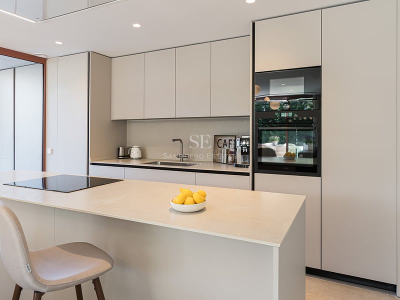 Modern sand-toned kitchen featuring a central island, integrated induction hob, and built-in designer appliances.