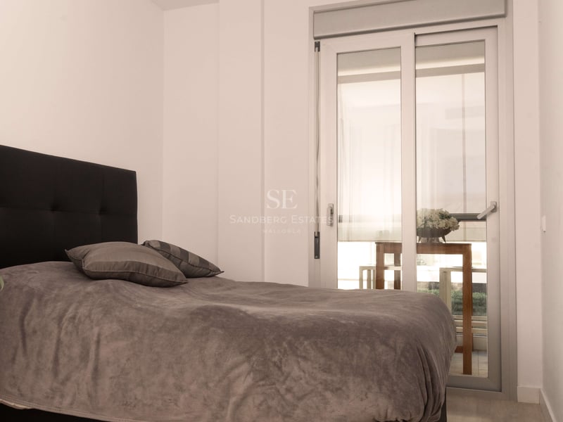 Schlafzimmer mit grauem Bett, schwarzem Kopfteil, hellem Holzboden und Glasschiebetür zur Terrasse.