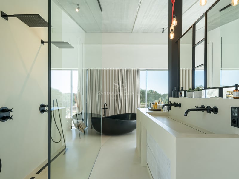 Minimalistiskt badrum med svart fristående badkar, dubbelhandfat och stora fönsterpartier.