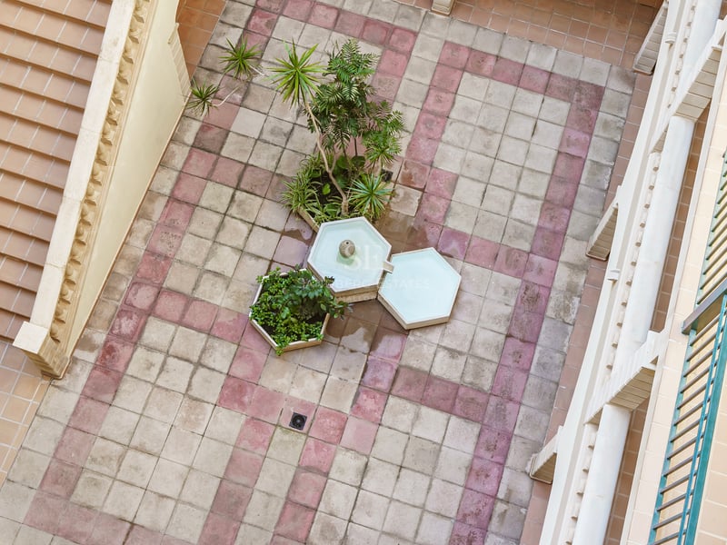 Flygvy över en stenlagd innergård med en hexagonal fontän, växter och en trappa.