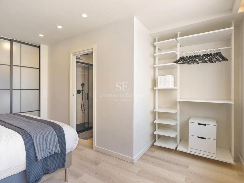 Helles modernes Schlafzimmer mit offenem weißem Schranksystem, hellem Echtholzparkett und Blick ins angrenzende Badezimmer.