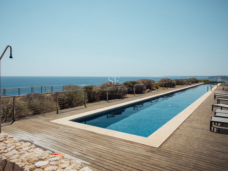 Longue piscine rectangulaire sur terrasse en bois surplombant la mer Méditerranée avec chaises longues et douche.
