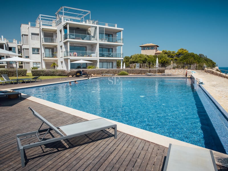 Grande piscine extérieure avec terrasse en bois, transats et immeuble d'appartements moderne par temps clair.