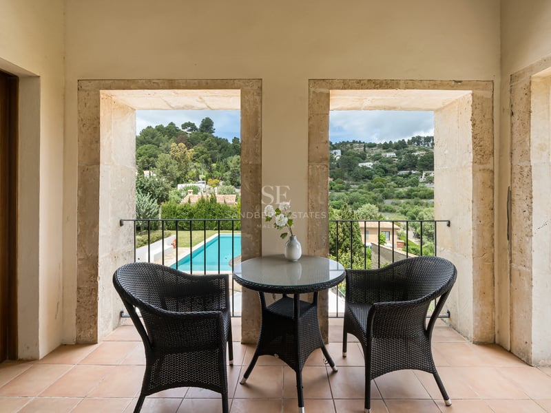 Deux chaises en osier et une table sur une terrasse encadrée de pierre avec vue sur une piscine et des collines vertes.