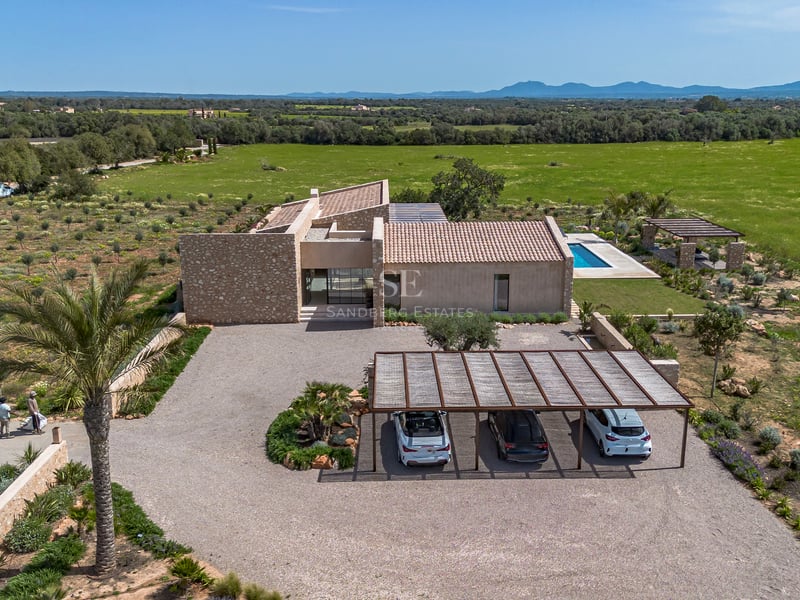 Luftaufnahme einer modernen Steinvilla mit Kiesauffahrt, Carport und Pool mit Blick auf die grüne Landschaft.