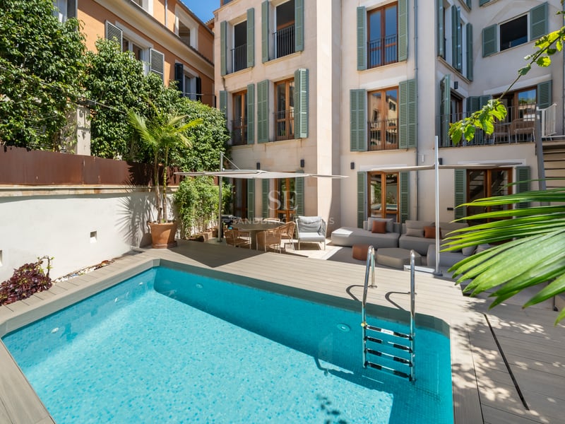 Une piscine turquoise dans une cour privée entourée d'un bâtiment à plusieurs étages avec des volets verts.