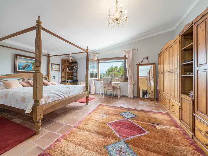 Chambre avec lit à baldaquin en bois, sol en terre cuite et grandes armoires sous un lustre en cristal.