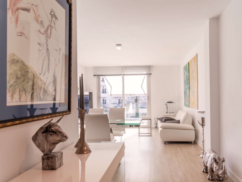 Modernes Wohn- und Esszimmer mit weißem Ledersofa, Glastisch und hellem Holzboden im natürlichen Tageslicht.