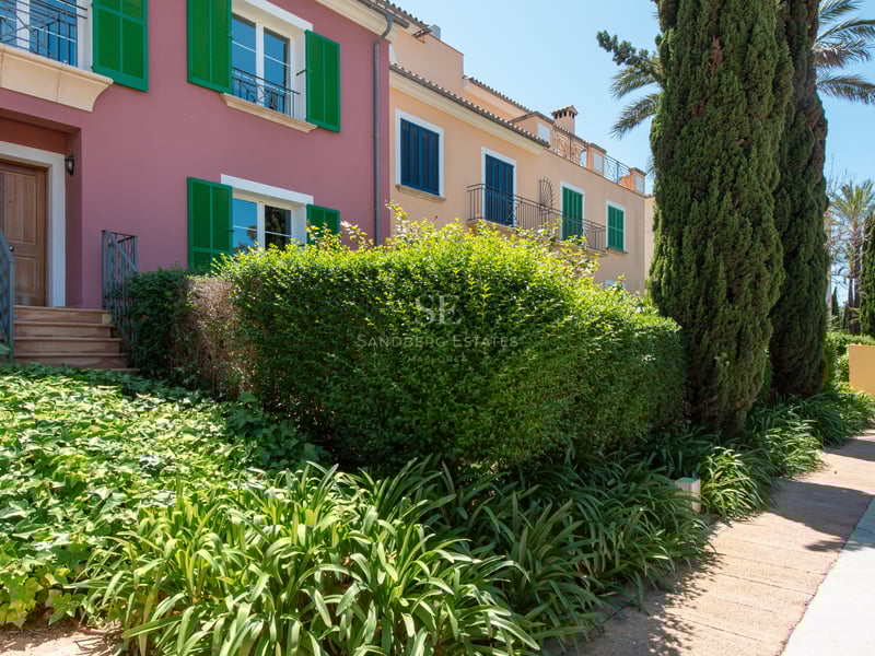 Colorful Mediterranean townhouses with green and blue shutters, surrounded by cypress trees and manicured gardens.