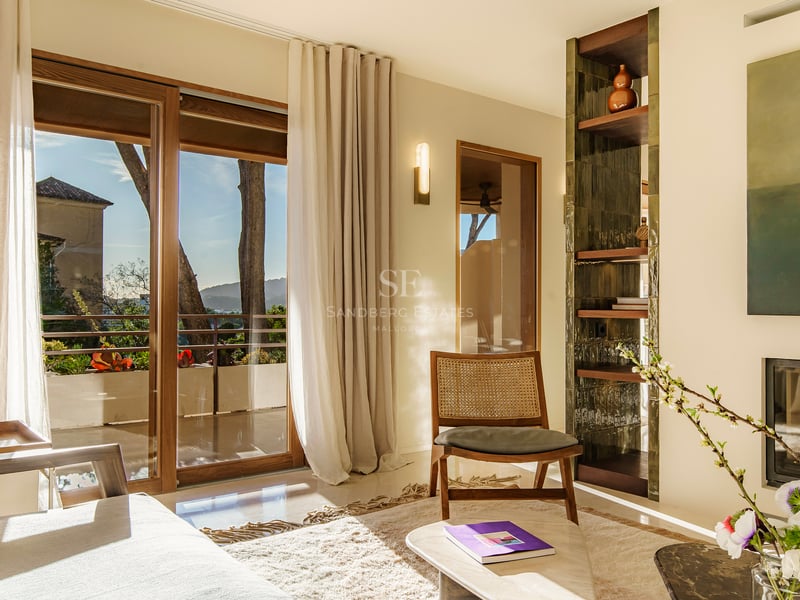 Lichtdurchflutetes Wohnzimmer mit Korbstuhl, Holzschiebetüren zum Balkon und eingebautem Kamin.