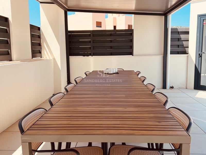 Une longue table à manger d'extérieur en bois avec dix chaises sous une pergola moderne sur une terrasse ensoleillée.