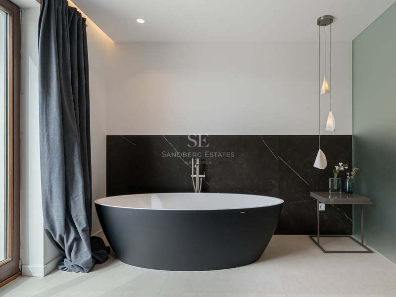 Salle de bain moderne avec baignoire îlot noire ovale devant un mur en marbre sombre et lumière naturelle.