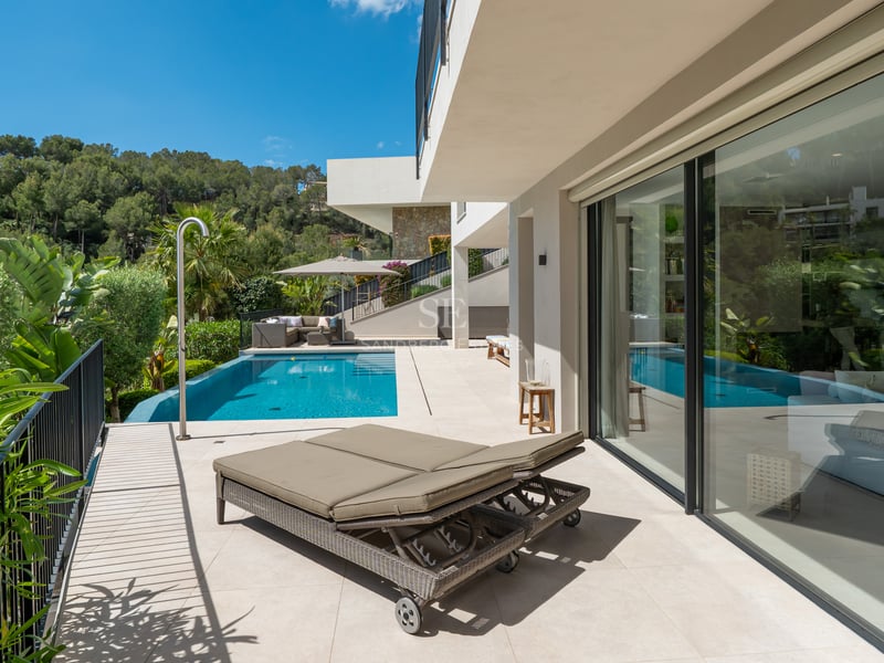 Vue sur la piscine avec terrasse en bois, chaises longues, parasols et jardin luxuriant. Design moderne avec éclairage naturel.