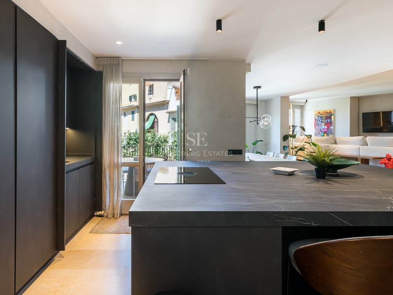 Cuisine contemporaine dotée d'un grand îlot en pierre noire, de rangements sombres et d'un sol en pierre claire.