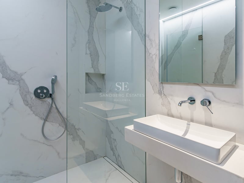 Salle de bain moderne avec carrelage effet marbre blanc, douche à l'italienne vitrée et lavabo minimaliste.