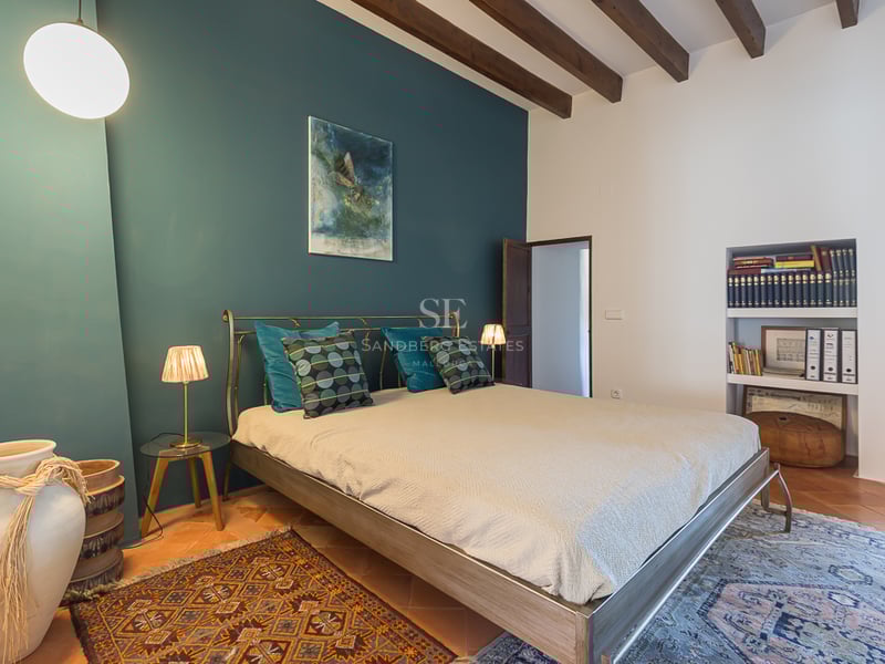 Chambre avec mur d'accent bleu canard, poutres en bois, sol en terre cuite et lit en métal.