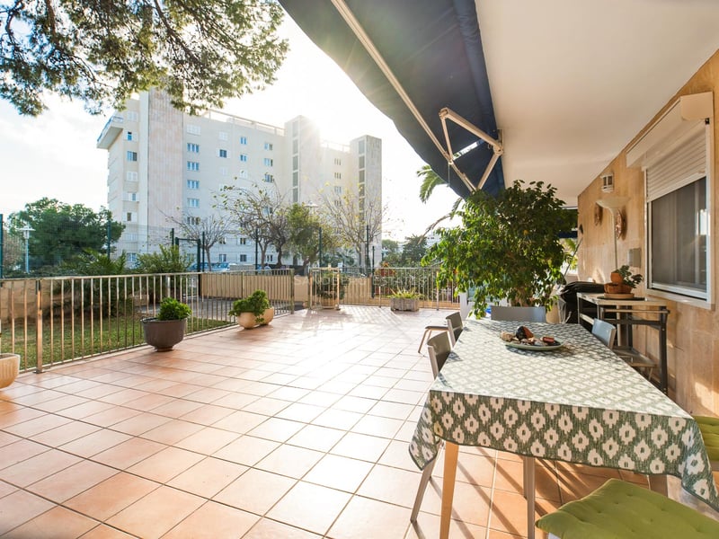 Weite Außenterrasse mit Terrakotta-Fliesen, Esstisch unter einer Markise und Natursteinwänden im Sonnenlicht.