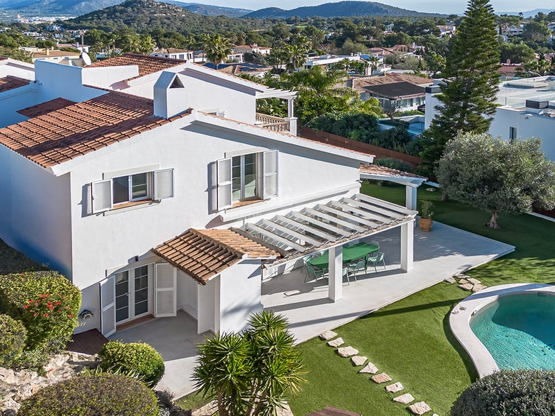 Flygvy över en vit villa med tegeltak, välskött trädgård, pergola och privat pool.