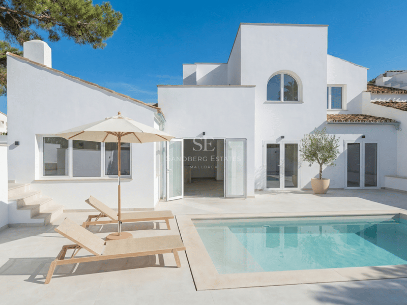 Villa contemporaine blanche avec piscine rectangulaire, terrasse en pierre claire et chaises longues sous un ciel bleu.