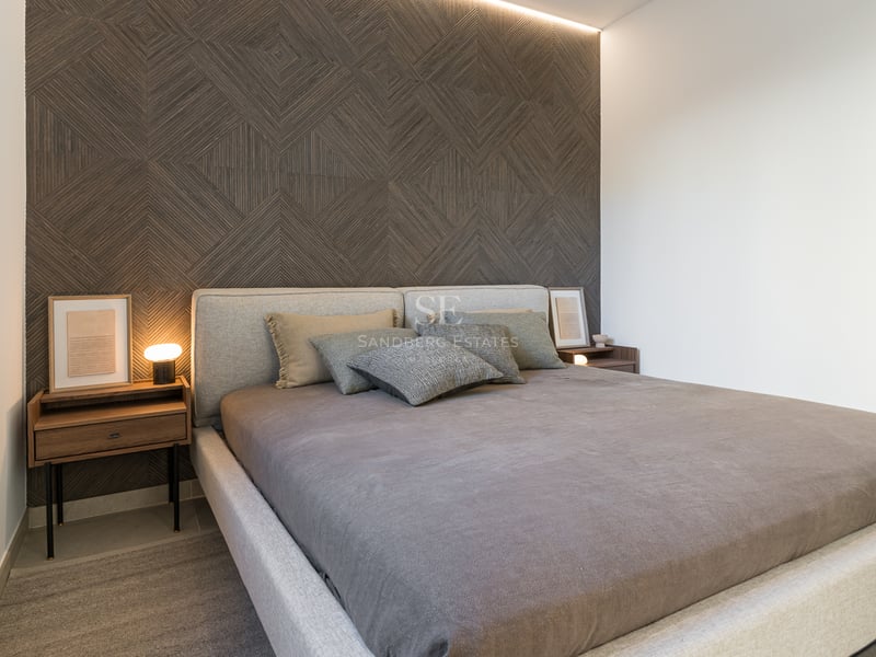 Ett modernt sovrum med en geometrisk fondvägg i trä, stoppad säng och nattduksbord i valnötsträ.