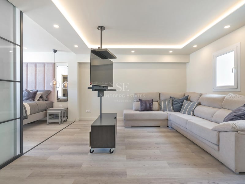 Zeitgenössisches Wohnzimmer mit großem beigem Ecksofa, drehbarem TV-Halter und angrenzendem Schlafbereich mit Glastrennwand.