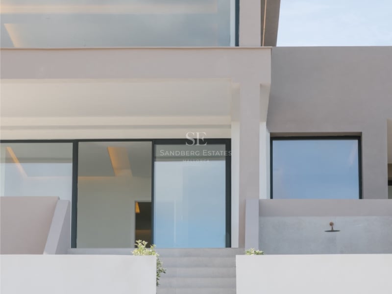 Außenansicht einer zeitgenössischen Villa mit Betontreppen, die zu großen Glasfronten und neutralen Wänden führen.