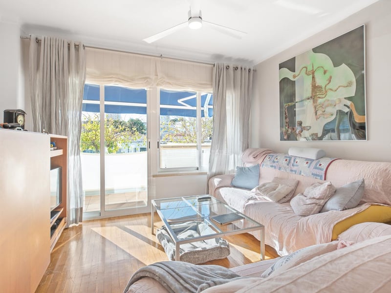 Lichtdurchflutetes Wohnzimmer mit Eichenparkett, Glastisch, rosa Sofa und Glasschiebetüren zum Balkon.