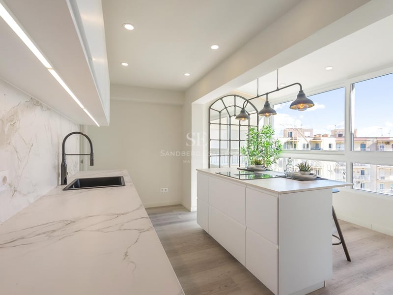 Moderne weiße Küche mit Marmor-Insel, industriellen Pendelleuchten und großen Fenstern mit Stadtblick.