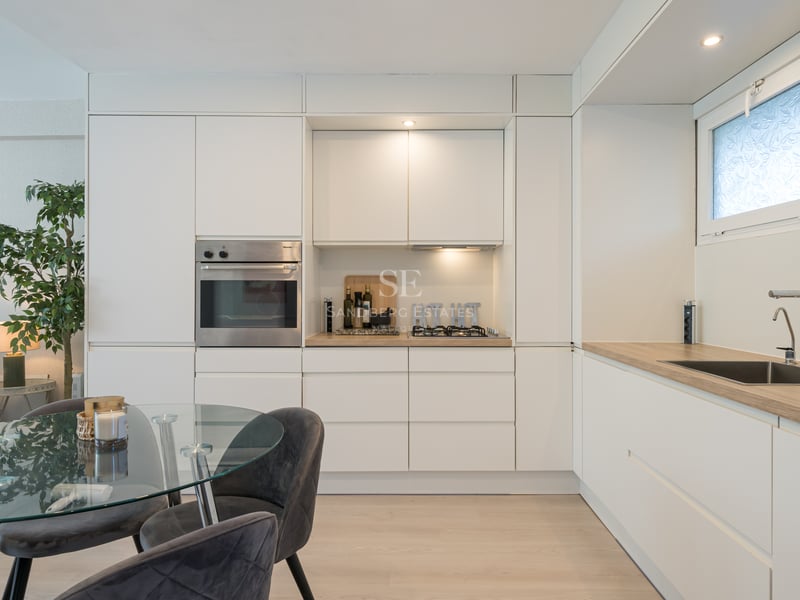 White minimalist kitchen with integrated Miele oven, wood-effect countertops, and a glass dining table with velvet chairs.