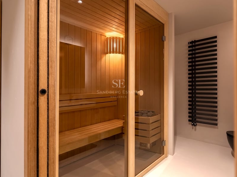 Sauna en bois clair avec porte vitrée, bancs à plusieurs niveaux et éclairage intérieur chaleureux.