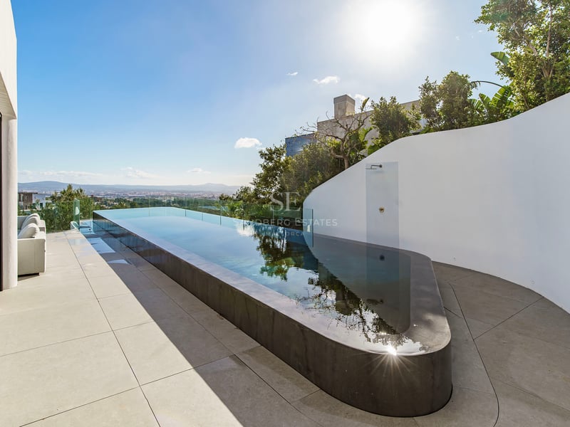 Une piscine à débordement élégante sur une terrasse blanche minimaliste surplombant la ville sous un ciel bleu.