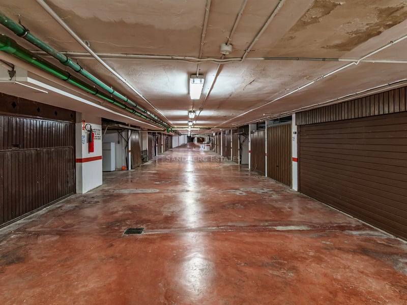 Underground garage hallway with red concrete floor and individual brown garage doors on both sides.