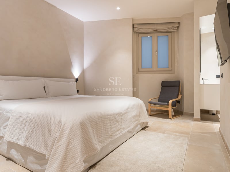 Chambre minimaliste avec sol en pierre naturelle, murs crème, grand lit et aperçu de la salle de bain.