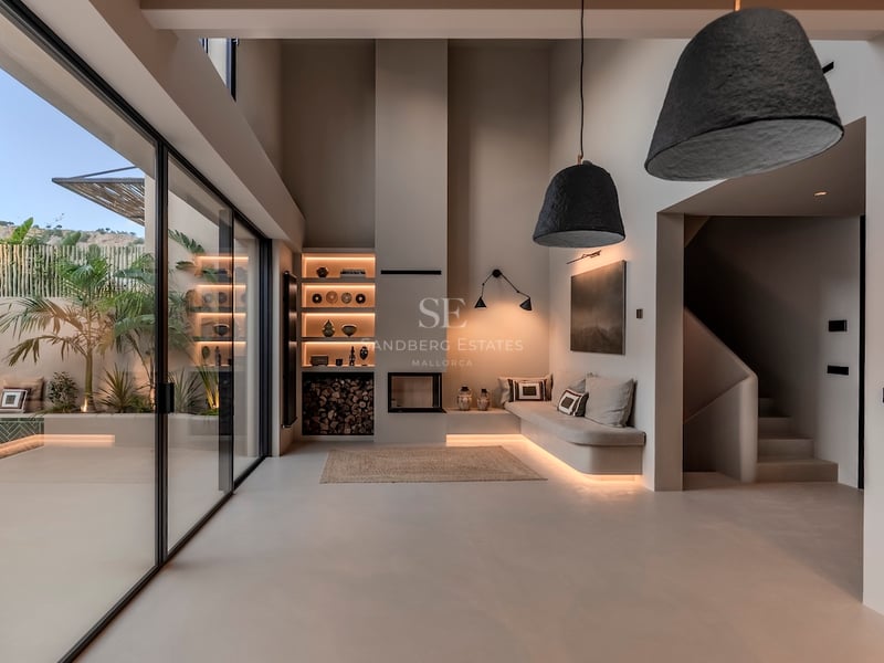 Salon minimaliste avec de hauts plafonds, un canapé intégré, une cheminée et de grandes baies vitrées sur un patio tropical.