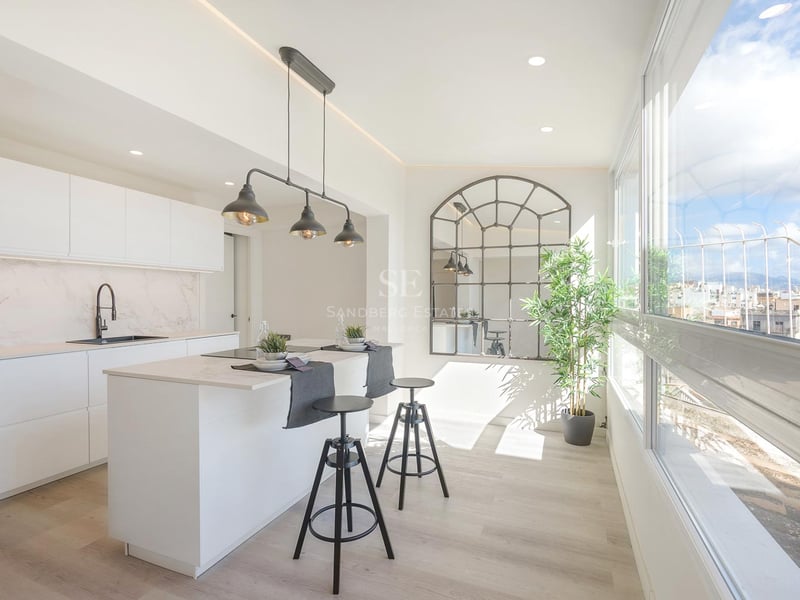 Helle moderne Küche mit weißer Kochinsel, schwarzen Barhockern und großen Fenstern mit Blick auf die Stadt.