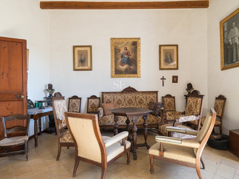 Un salon classique avec des meubles en bois anciens, des tissus d'ameublement à motifs, des peintures religieuses et un sol en carrelage.