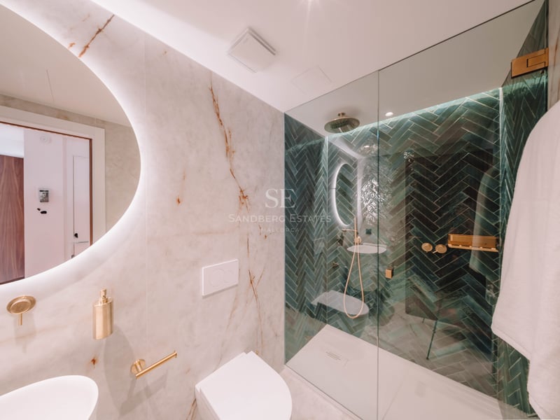 Salle de bain moderne avec murs en marbre, miroir rond rétroéclairé et douche avec carreaux verts en chevrons.