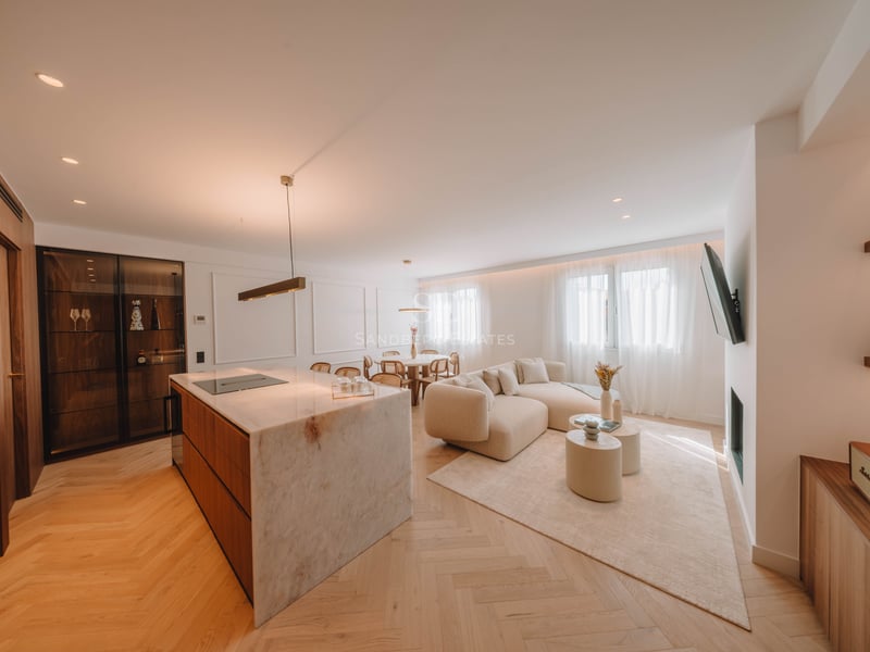 Salon lumineux à aire ouverte avec un grand îlot de cuisine en marbre, un canapé beige incurvé et un parquet en chevrons.