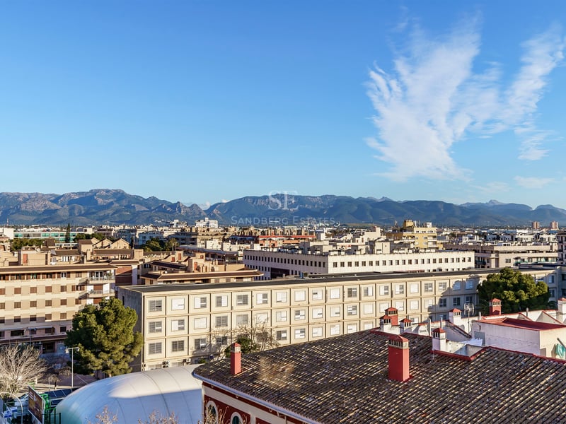 Vue surélevée sur les toits de la ville vers une chaîne de montagnes lointaine sous un ciel bleu.