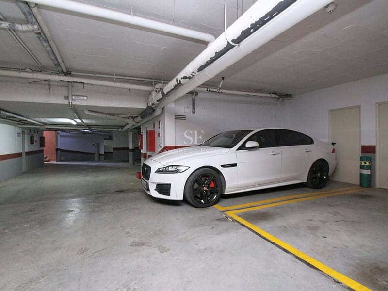 En vit bil parkerad i ett ljust underjordiskt garage med betonggolv och gula parkeringslinjer.