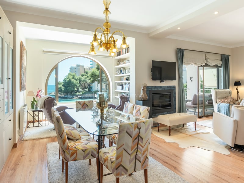 Ljus matsal med glasbord och ett stort bågfönster med utsikt över havet och kustlandskapet.