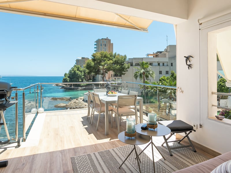 Solig terrass med glasräcke och utsikt över Medelhavet, inredd med matplats för sex personer.