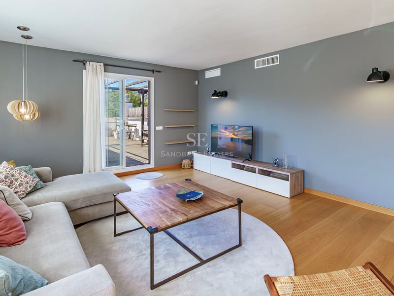 Ljust vardagsrum, grå väggar, ekparkett, hörnsoffa och glasdörr mot en träterrass.