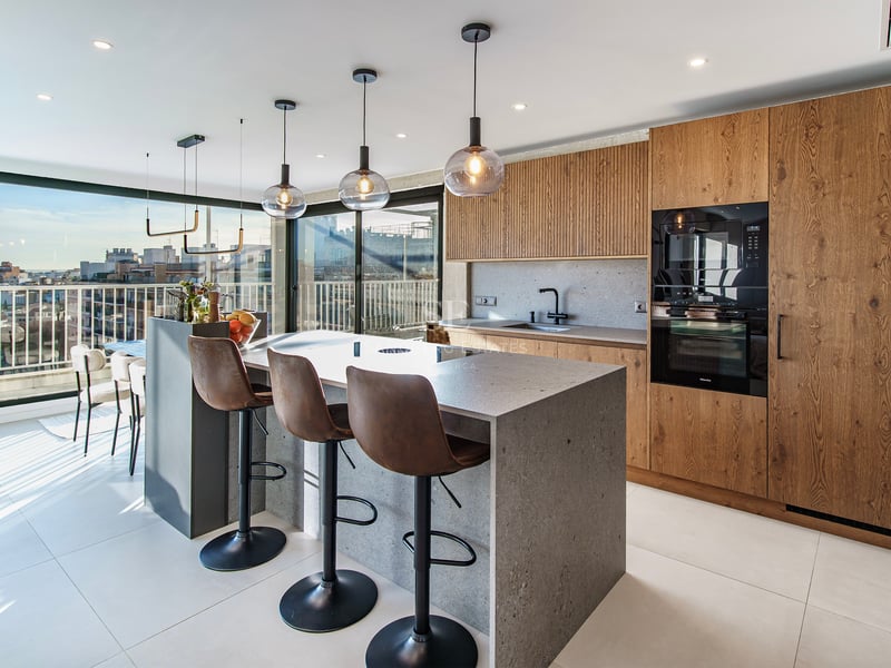 Cuisine moderne avec îlot en pierre, tabourets en cuir et grandes fenêtres offrant une vue panoramique sur la ville.