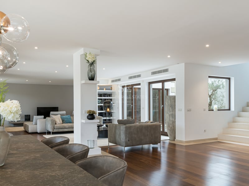 Intérieur spacieux avec parquet foncé, table de salle à manger en pierre, luminaire globe et escalier en pierre blanche.