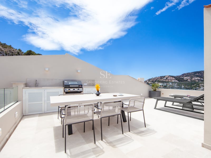 Terrasse moderne sur le toit avec cuisine extérieure, table à manger et transats avec vue panoramique.