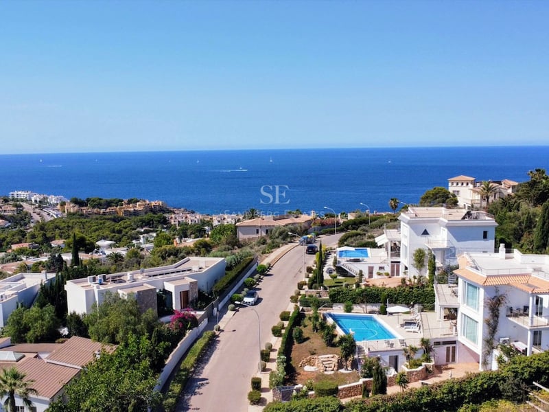 Vue aérienne de villas de luxe blanches avec piscines donnant sur la mer Méditerranée sous un ciel bleu clair.