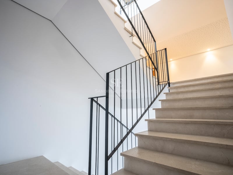 Cremefarbene Marmortreppe mit schwarzem Eisengeländer vor weißen Wänden bei natürlichem Licht.