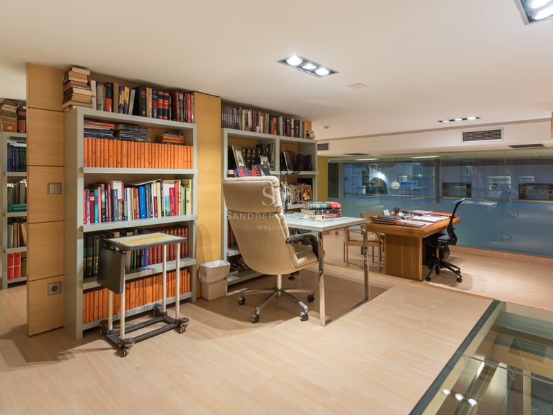 Bureau moderne avec parquet clair, étagères intégrées, bureau en verre et fauteuil ergonomique en cuir.