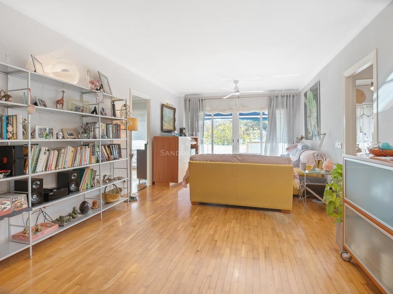 Großzügiges Wohnzimmer mit honigfarbenem Eichenparkett, großem Metallregal und Glasschiebetüren zum Balkon.